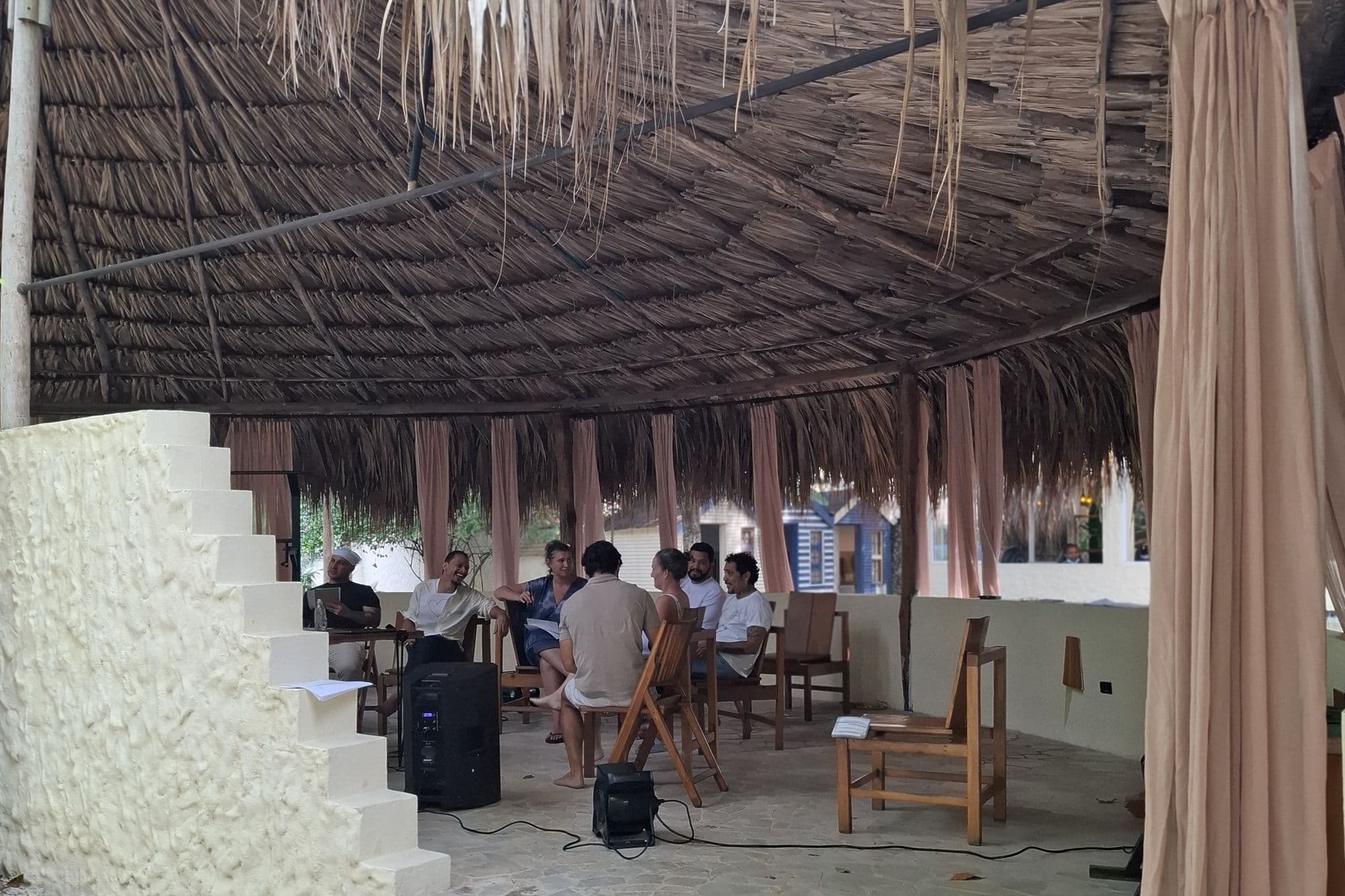 A Scandinavian Collective Wellness programme in session with the Blue Apple team, gathered in a circle under a palm-thatched kiosco.